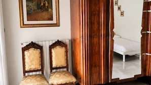 A room with a wooden wardrobe, two upholstered chairs, a bed, and a framed painting on the wall. - Historic Stay Near the Sassi of Matera (Matera)