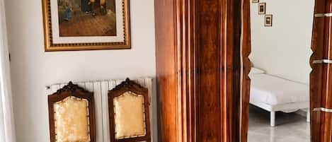 Una habitación con un armario de madera, dos sillones tapizados, una cama y un cuadro enmarcado en la pared.
