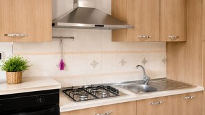 A modern kitchen with wooden cabinets, a stainless steel range hood, a gas stove, and a sink. - Historic Stay Near the Sassi of Matera (Matera)