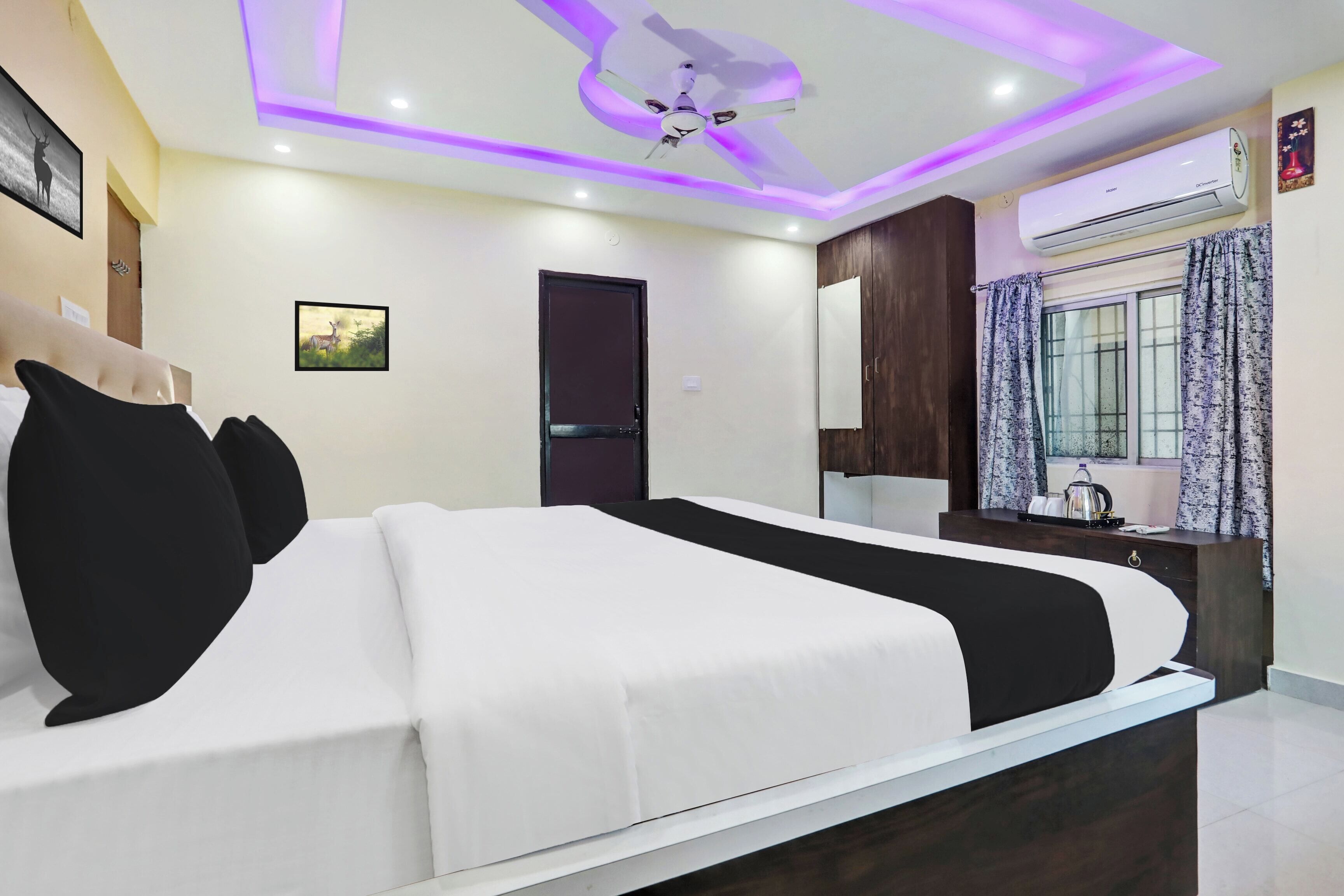 A hotel room with a bed, a ceiling fan, an air conditioning unit, a window with curtains, and a mirror.