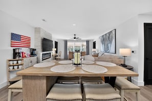 A modern living room with a dining area, a fireplace, and a large window. - Bama Oasis | 3 Private Suites | Pool & Fitness Center (Tuscaloosa)