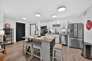 Une cuisine moderne avec des meubles blancs, un réfrigérateur en acier inoxydable et un coin repas comprenant une table et des chaises en bois.