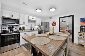 A modern kitchen with white cabinets, a stainless steel range, and a wooden dining table with placemats.