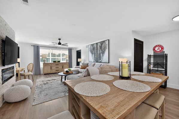 A modern living room with a wooden dining table, a sofa set, and a large framed artwork.
