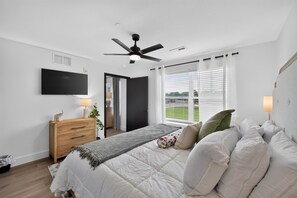 A bedroom with a bed, bedside lamps, a ceiling fan, a TV, and a window with blinds.