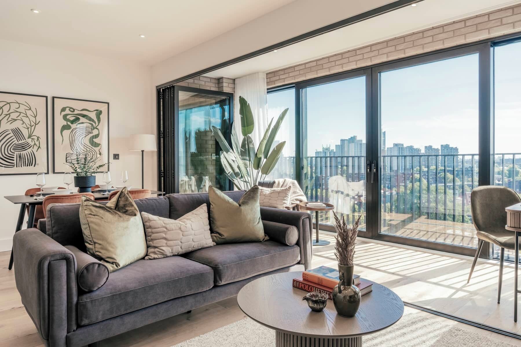 A modern living room with a grey sofa, a round coffee table, and a city view through large windows.