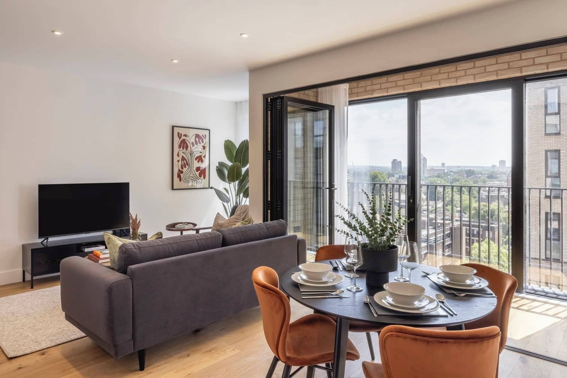 A modern living room with a sofa, TV, and dining table set for four.