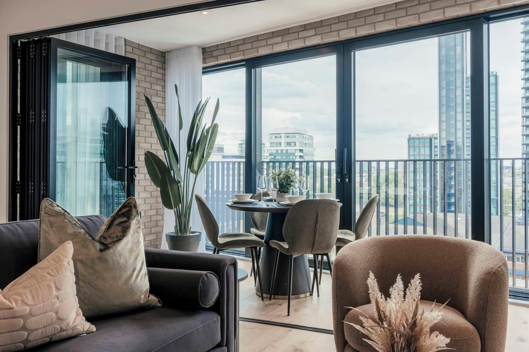 A modern living room with a sofa, chairs, a dining table, and a balcony with a city view.