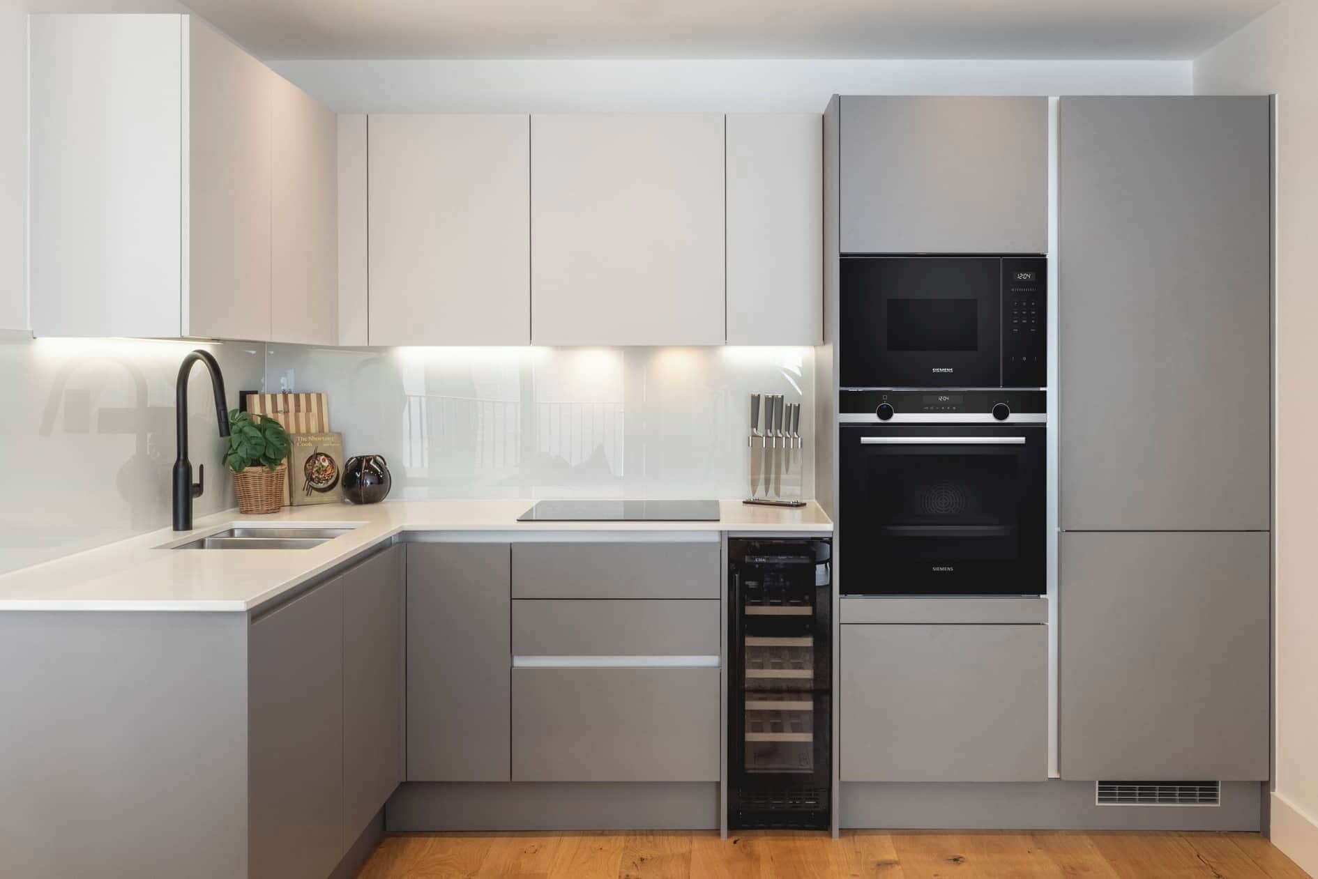 Una cocina moderna con armarios grises, un lavamanos de acero inoxidable, un horno empotrado y un microondas.