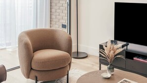 A modern living room with a beige armchair, a round coffee table, a black TV stand, and a vase with dried plants. - Urban Rest Albert Embankment (London)