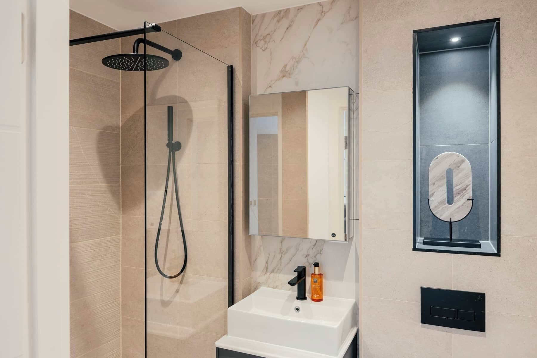 A modern bathroom with a glass-enclosed shower, a white sink, and a mirror with a marble-like design.