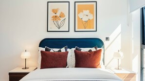 A bedroom with a bed, two bedside tables, a window, and two framed floral artworks on the wall. - Urban Rest Albert Embankment (London)
