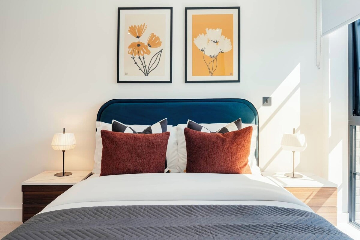 Ein Schlafzimmer mit einem Bett, zwei Nachttischen, einem Fenster und zwei gerahmten Blumenbildern an der Wand.