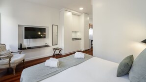 Ein modernes Hotelzimmer mit einem großen Bett, einem flachbildfernseher an der Wand, einem kleinen Nachttisch und einem Sessel.