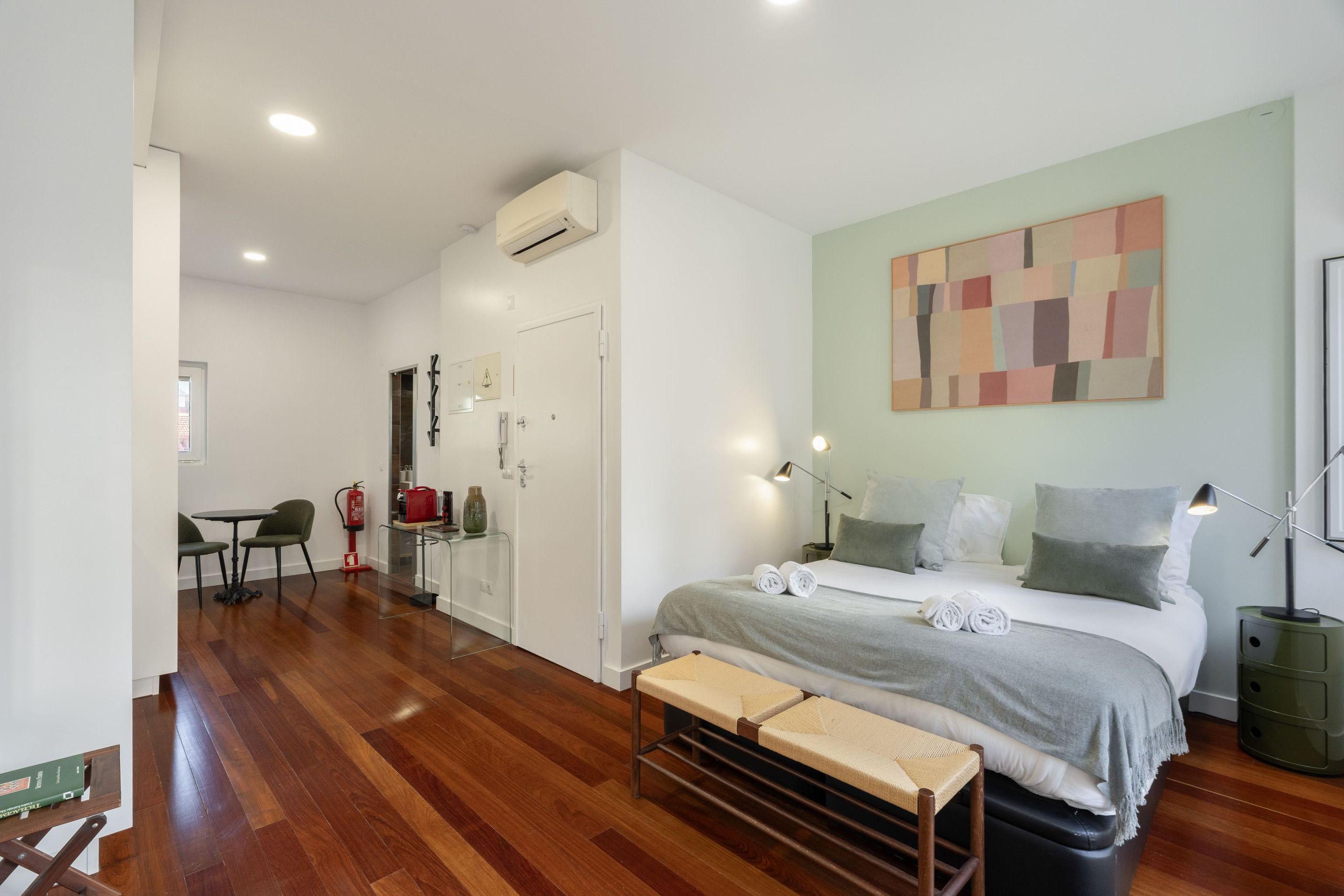 Una habitación de hotel moderna con cama, lámparas de noche, un banco y un cuadro en la pared.