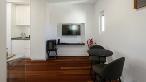 Ett modernt och kompakt bostadsutrymme med kök, matplats och en väggmonterad platt-TV.