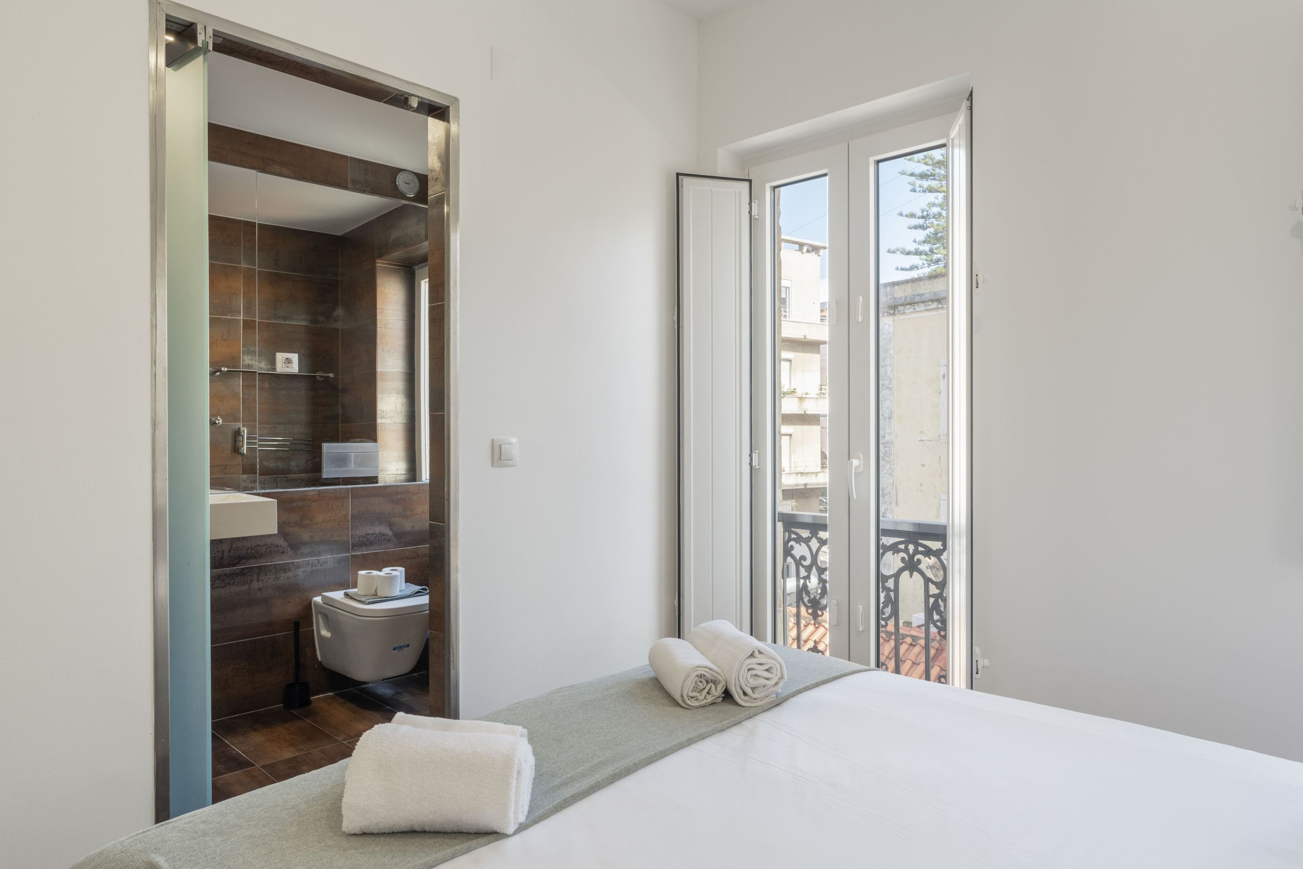 A hotel room with a bed, a bathroom, and a balcony with a view.
