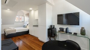 A modern bedroom with a bed, a desk with a computer, a TV, and a window with a view of the roof. - Estrela Riverside Studios IV by Homing (Lisbon)
