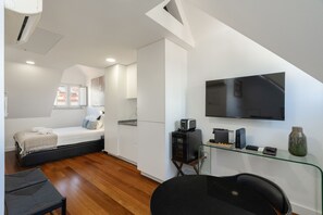 Un dormitorio moderno con una cama, un escritorio con una computadora, un televisor y una ventana con vistas al tejado.