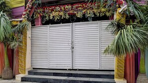 Une porte double fermée, surmontée d’une composition florale, flanquée de palmiers, et un escalier menant à la porte.