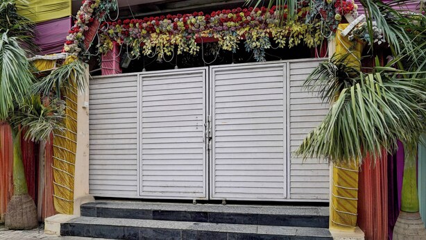Una puerta doble cerrada con un arreglo floral en la parte superior, flanqueada por plantas de palma, y una serie de escalones que conducen a la puerta.