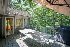 A covered deck with a table and chairs, a grill, and a view of a wooded area. - King Bed: Deck w/Grill: Fireplace: Smart TVs: Pool + Gym Access: EV Level 2 (Galena)