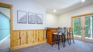 A room with a wooden panel wall, a dining area with a table and chairs, and a large window with a view of greenery. - King Bed: Deck w/Grill: Fireplace: Smart TVs: Pool + Gym Access: EV Level 2 (Galena)