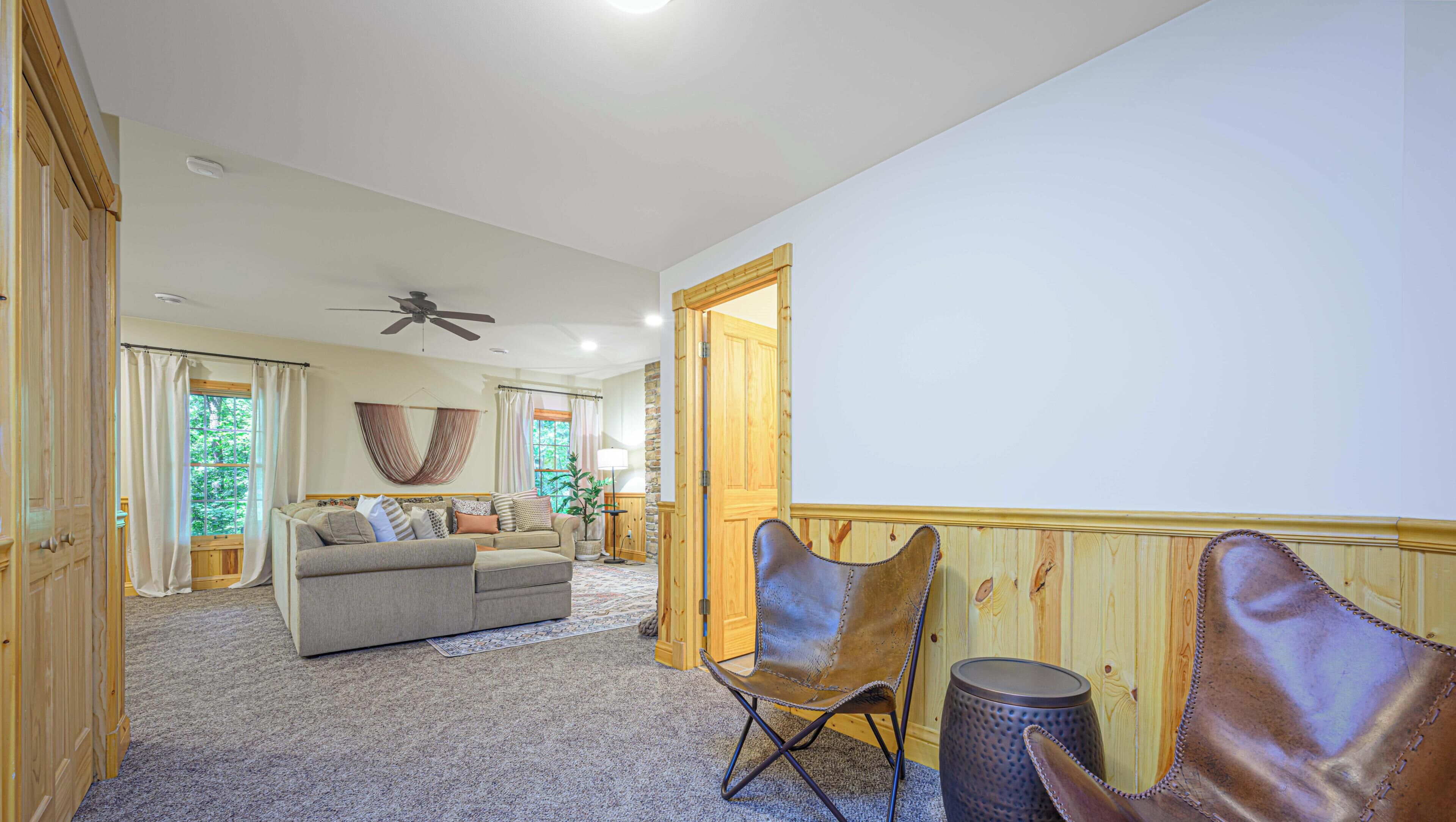 A spacious living room with a sofa, chairs, a ceiling fan, and a large window.