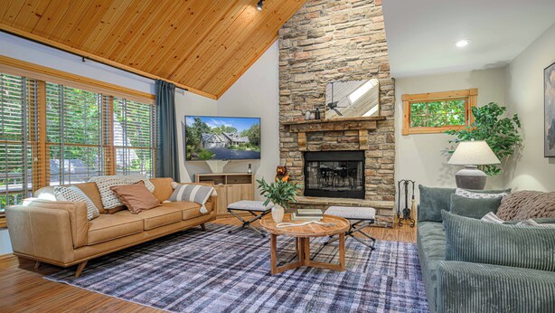 A spacious living room with a stone fireplace, wooden ceiling, and large windows. - King Bed: Deck w/Grill: Fireplace: Smart TVs: Pool + Gym Access: EV Level 2 (Galena)