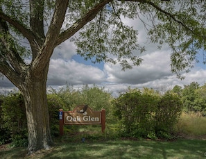 Ein hölzernes Schild mit der Aufschrift 'Oak Glen', umgeben von Bäumen und Grünpflanzen.