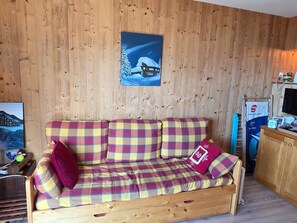 A wooden-paneled room with a plaid sofa, a painting of a snowy landscape, and a small kitchenette area. - Apartment with great view, 4 guests (Avoriaz)