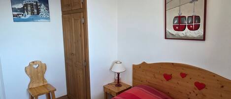 Une chambre à coucher comprenant un lit, une chaise en bois, une table de chevet, une lampe et deux œuvres d’art accrochées au mur.