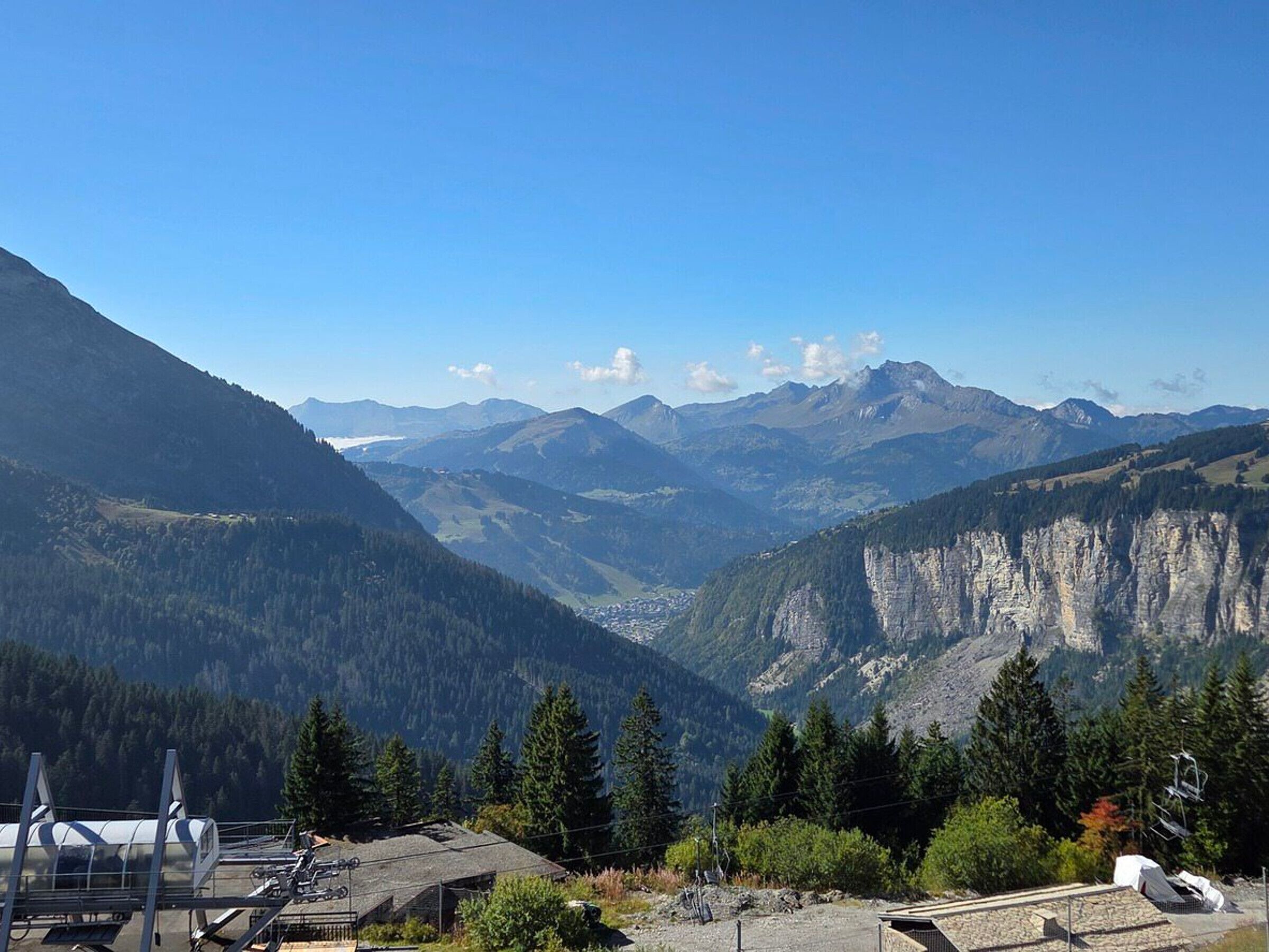 A mountainous landscape with a clear sky, a valley, and a building with a sloped roof and solar panels.