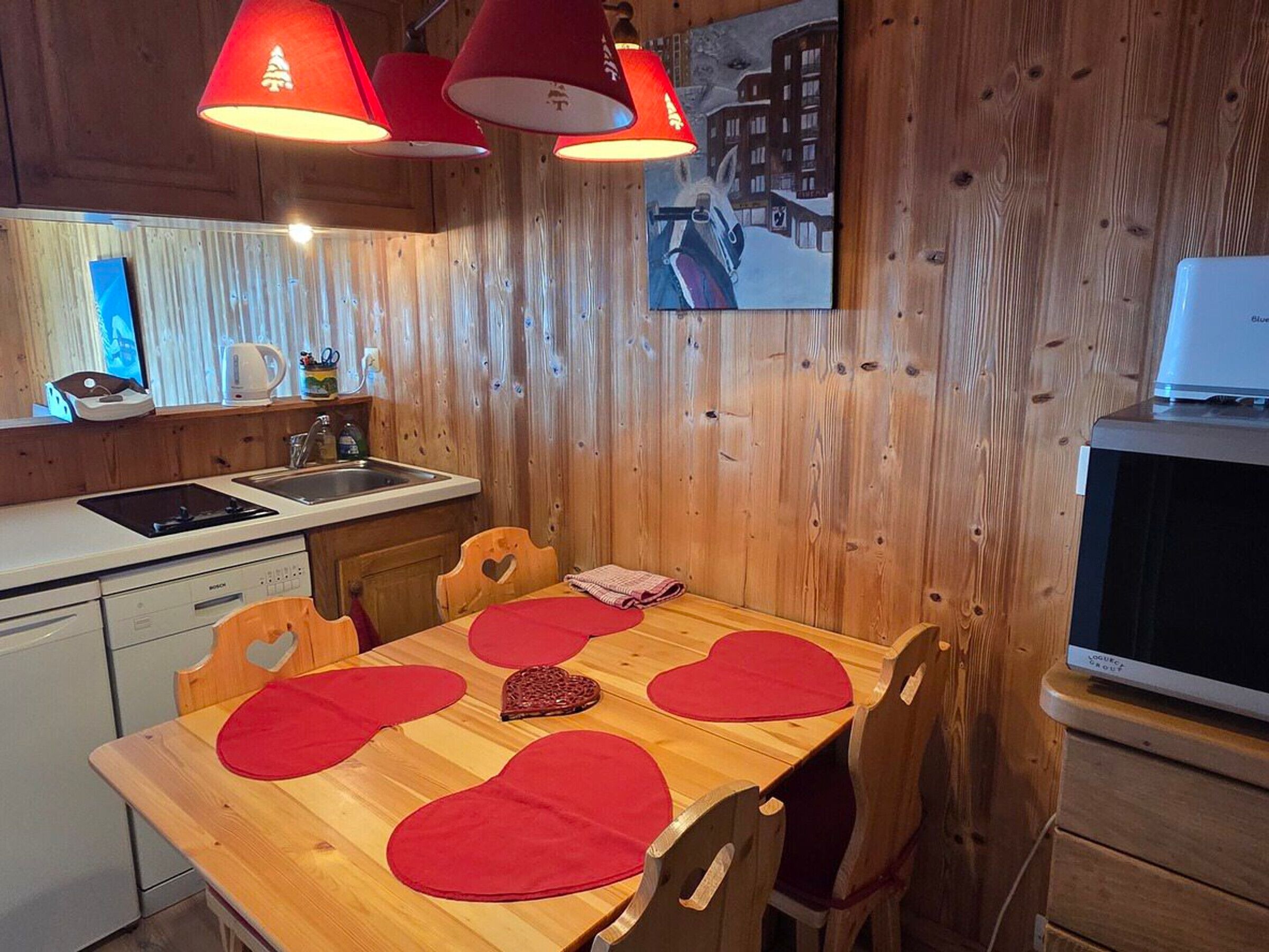 A wooden interior with a kitchen area, a dining table with heart-shaped placemats, and a painting on the wall.