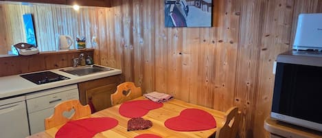 A wooden interior with a kitchen area, a dining table with heart-shaped placemats, and a painting on the wall.