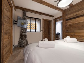 Ein Schlafzimmer mit einem großen Bett, Holzwänden, einem an der Wand montierten Fernseher und einem Fenster mit Vorhängen.