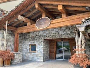 A stone building with a wooden facade, a sign above the entrance, and two large potted plants. - Panoramic view apartment, pets allowed - 8 guests (Val-d'Isère)