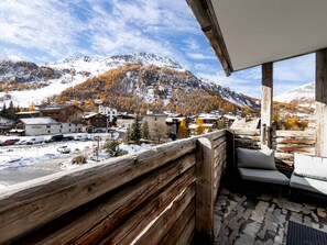 Ein Holzbalkon mit Blick auf eine verschneite Bergstadt und herbstlich gefärbte Bäume.