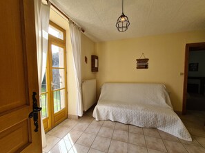 Ein Zimmer mit einem Bett, einem Heizkörper, einer Hängelampe und einem Fenster mit Vorhängen.