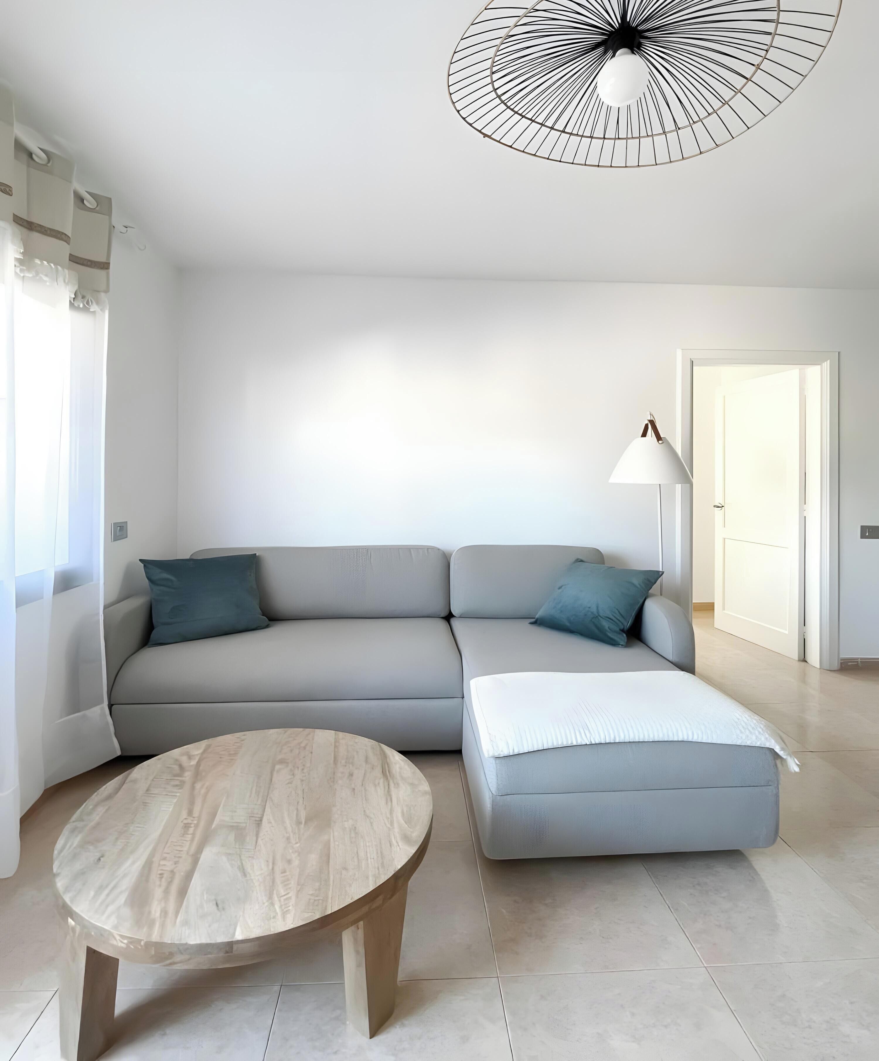 Una sala de estar moderna con un sofá gris, una mesa de centro de madera redonda y una lámpara de pie.