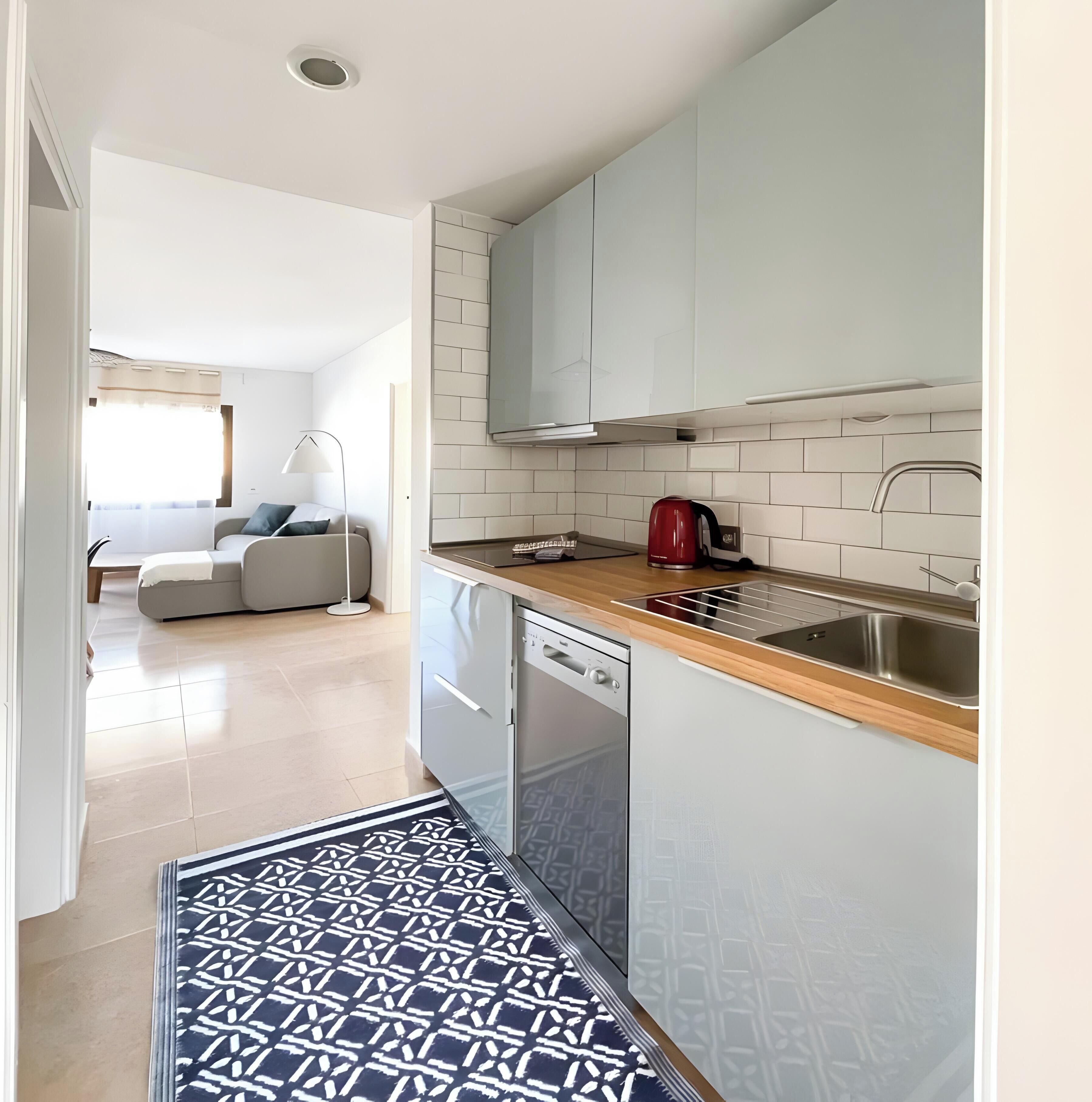 Una cocina moderna con armarios blancos, un lavamanos de acero inoxidable y un hervidor rojo.