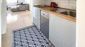 Une cuisine moderne avec des meubles blancs, un évier en acier inoxydable et une bouilloire rouge.