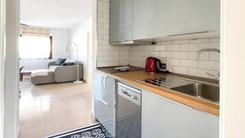Una cocina moderna con armarios blancos, un lavamanos de acero inoxidable y un hervidor rojo.