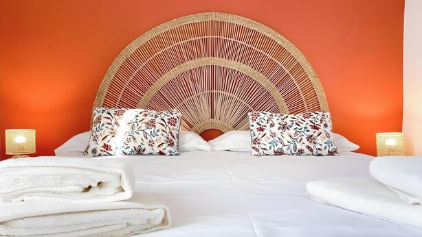 Un lit avec une tête de lit en osier, deux oreillers à motifs floraux et deux lampes de chevet.