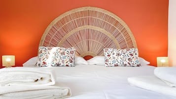 Una cama con cabecera de fibras naturales, dos almohadas con motivos florales y dos lámparas de noche.