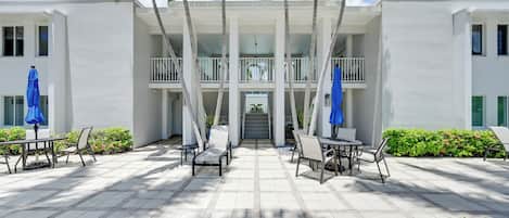 A hotel with a covered outdoor seating area, palm trees, and a two-story building.