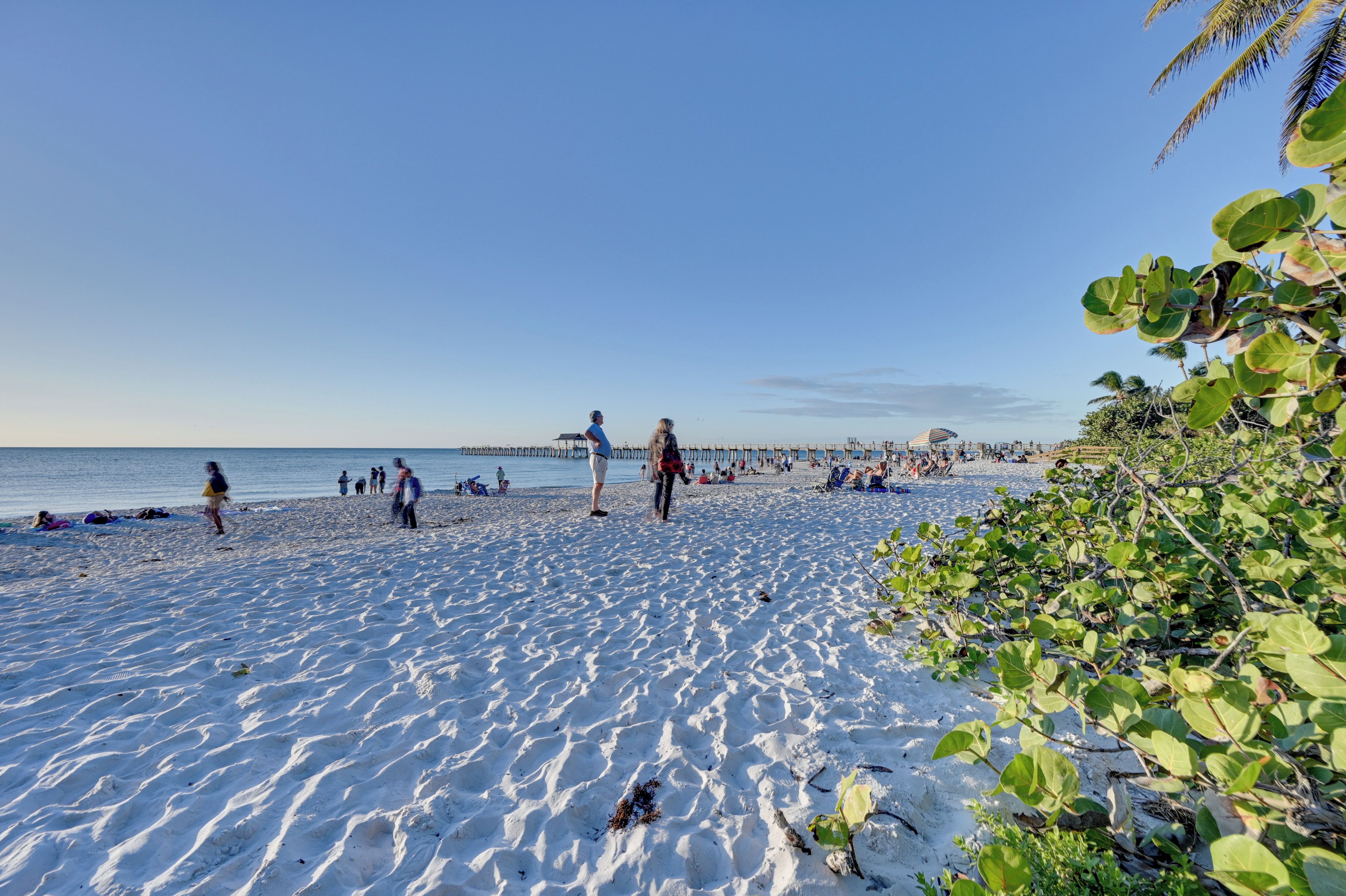 A beach with people, a pier, and a clear sky.