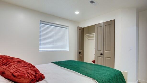A bedroom with a bed, a window with blinds, and a door leading to another room.