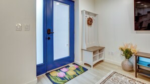 A hallway with a blue door, a white coat closet, a wooden bench, and a floral doormat.
