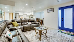 A modern living room with a leather sofa, a glass coffee table, and a dining area in the background.